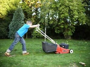 caucasian child pushing a push mower